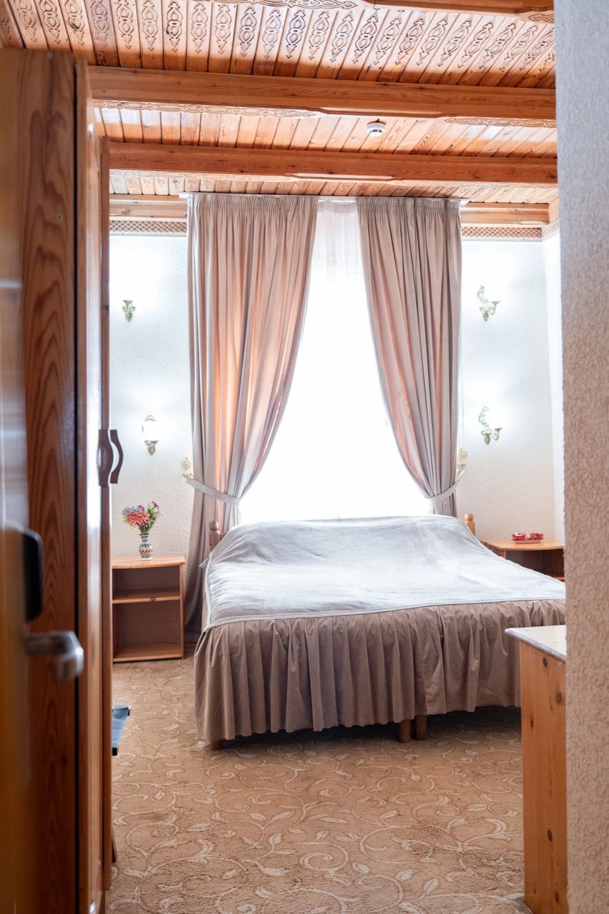 Ein Schlafzimmer mit Bett, Vorhängen, einem Nachttisch und einer Wandlampe.