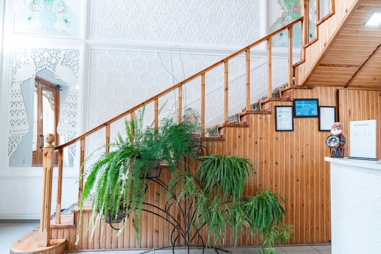 Uma escadaria de madeira com corrimão, cercada por plantas em vasos e certificados emoldurados na parede.