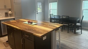 Une cuisine avec un îlot central en bois, deux pommes posées sur un set de table, une table à manger avec des chaises et une fenêtre avec des stores.