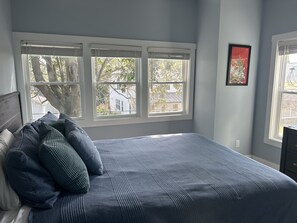 Un dormitorio con una cama grande, tres ventanas y un cuadro en la pared.