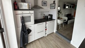 A compact kitchen with white cabinets, a microwave, an oven, and a toaster. There is a small dining area with a white chair and a table. - Stylish 1-bed Studio in Humberston, Cleethorpes (Grimsby)