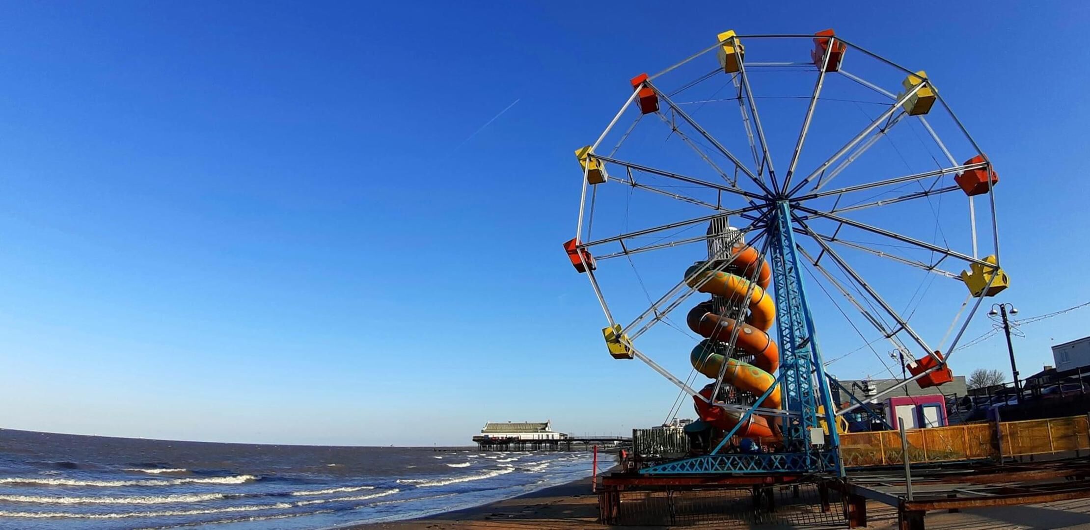 Ein Riesenrad mit bunten Gondeln direkt am Strand.