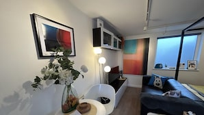 A modern living room with a sofa, a dining table with a vase of flowers, and a painting on the wall. - Stylish 1-bed Studio in Humberston, Cleethorpes (Grimsby)