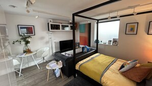 A modern bedroom with a four-poster bed, a desk with a chair, a small table with a vase, and a TV. - Stylish 1-bed Studio in Humberston, Cleethorpes (Grimsby)
