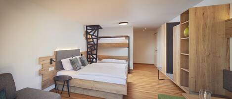 A modern hotel room with a bunk bed, a small sofa, a round table, and a wooden bookshelf.
