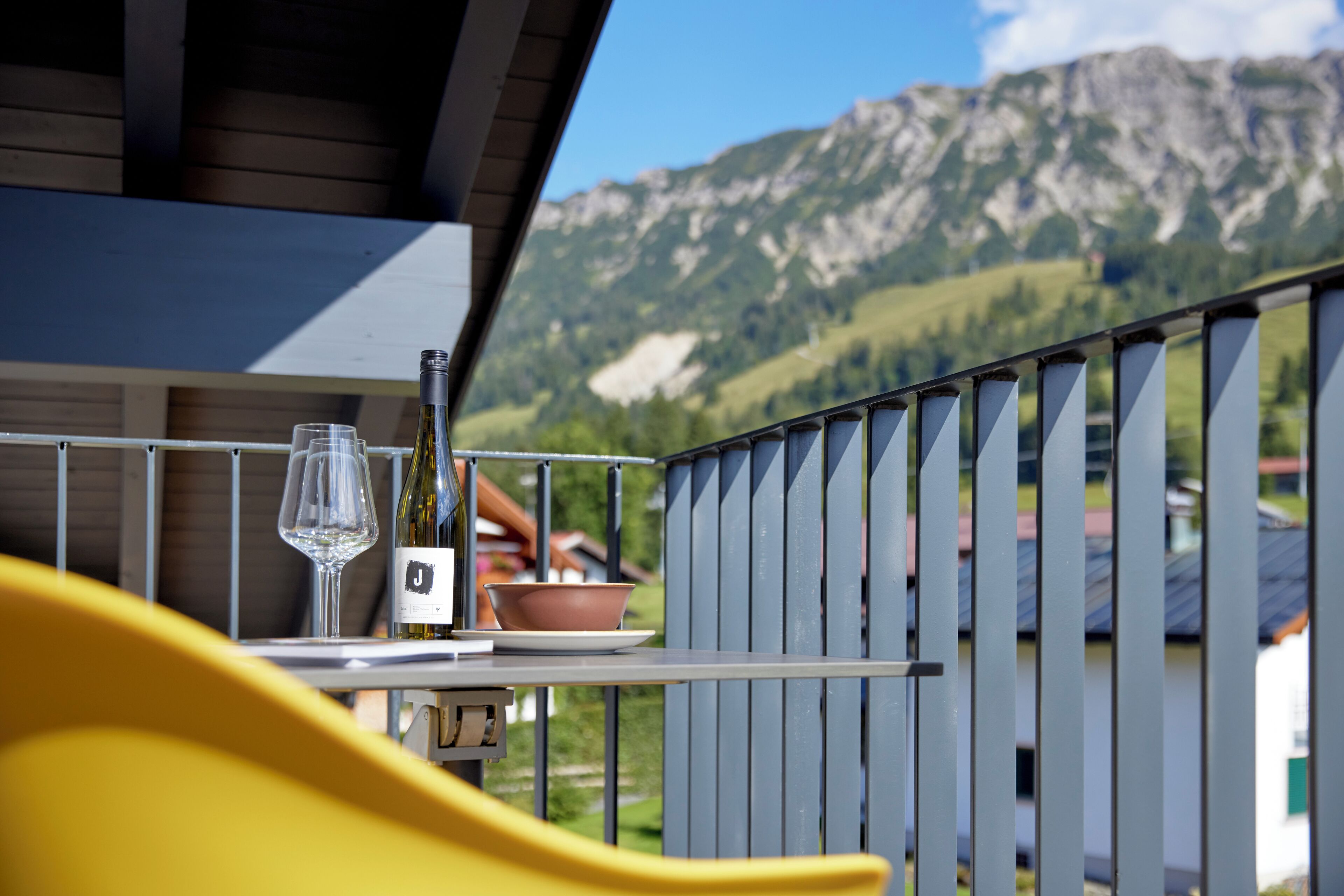 A balcony with a table, a wine glass, and a bottle, overlooking a mountainous landscape.