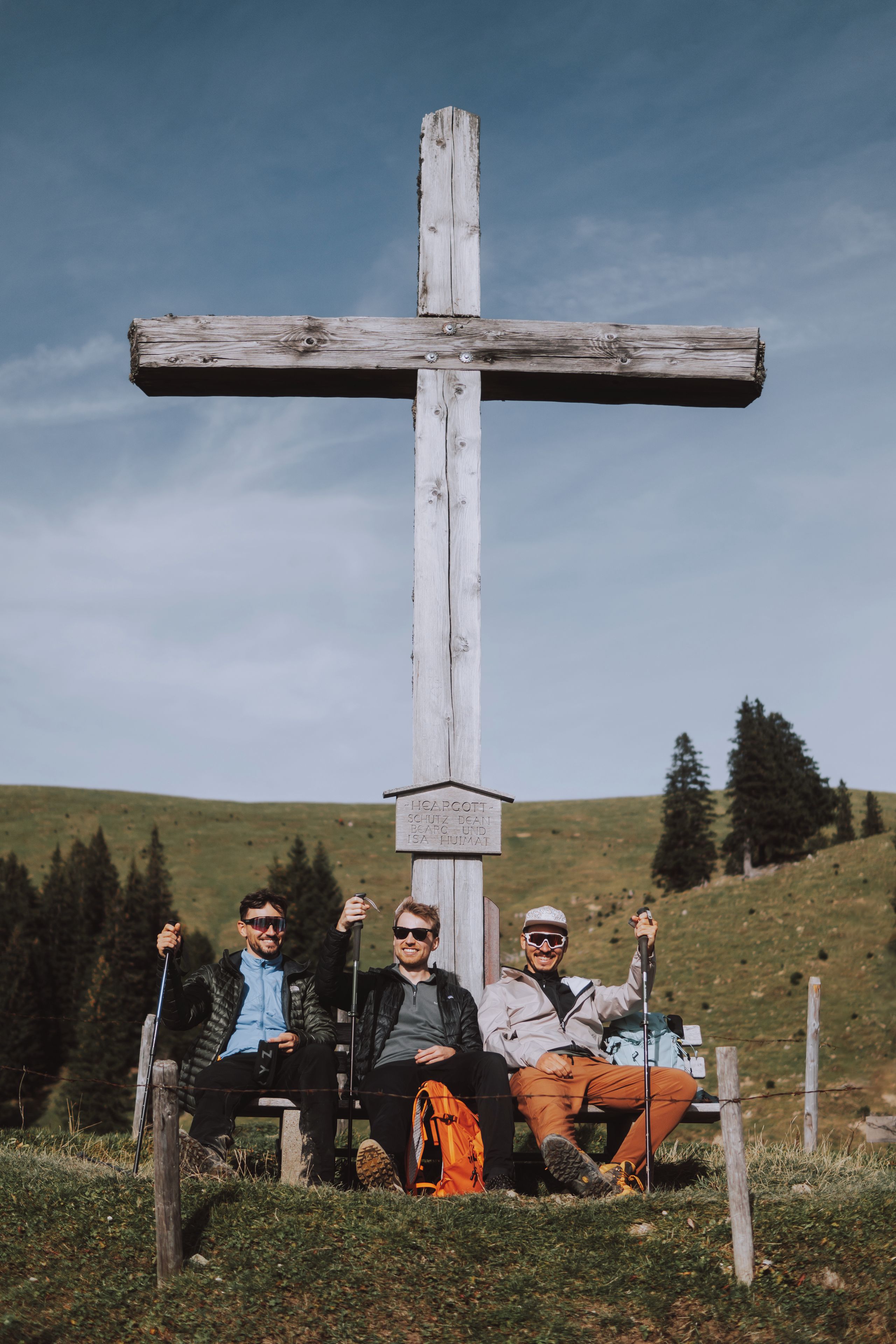 Three people sitting on a bench with a wooden cross in the background.