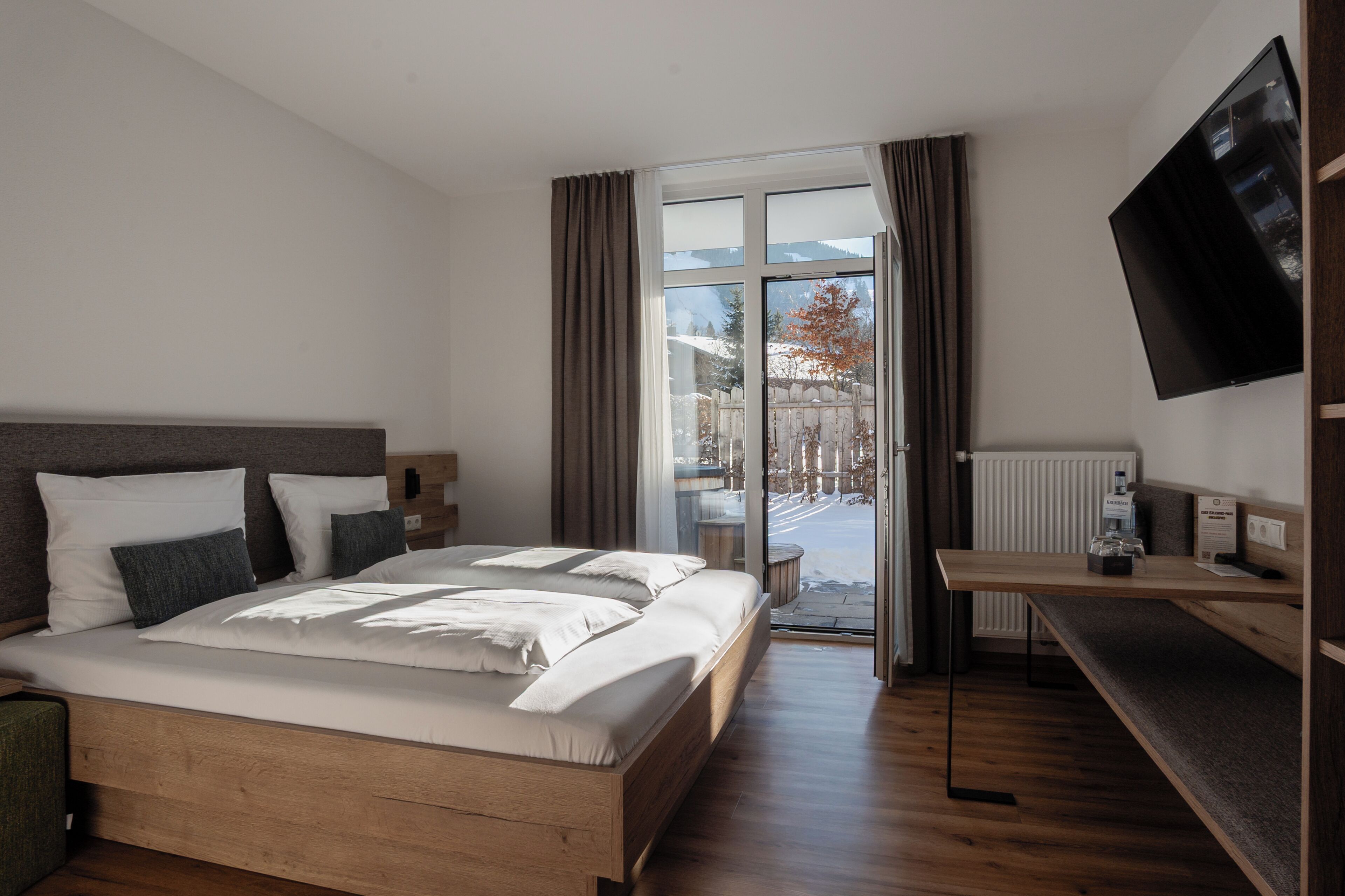 A modern hotel room with a large bed, a desk, a flat-screen TV, and a view of a snowy landscape through the window.