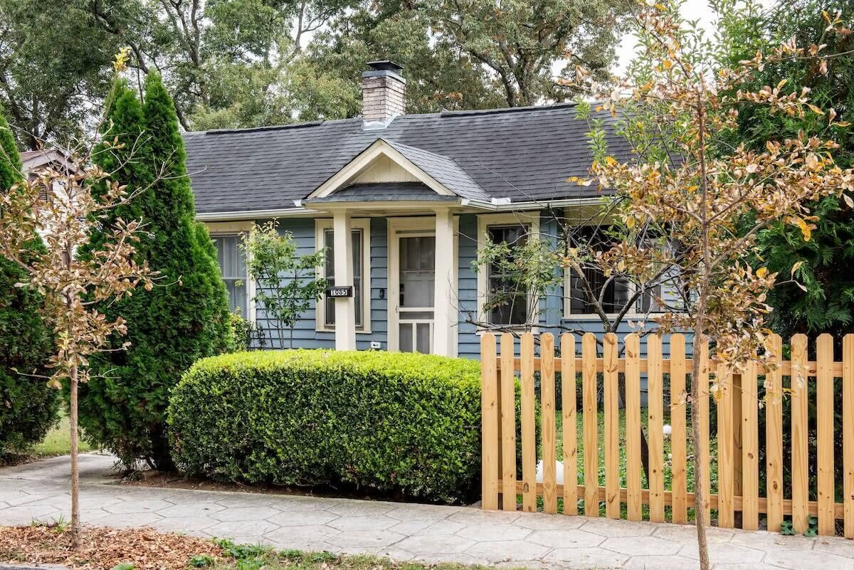 A two-story house with a front porch, a picket fence, and a well-maintained hedge.
