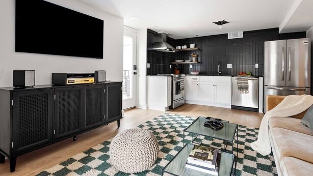 A modern kitchen with dark cabinetry, stainless steel appliances, and a flat-screen TV mounted on the wall.