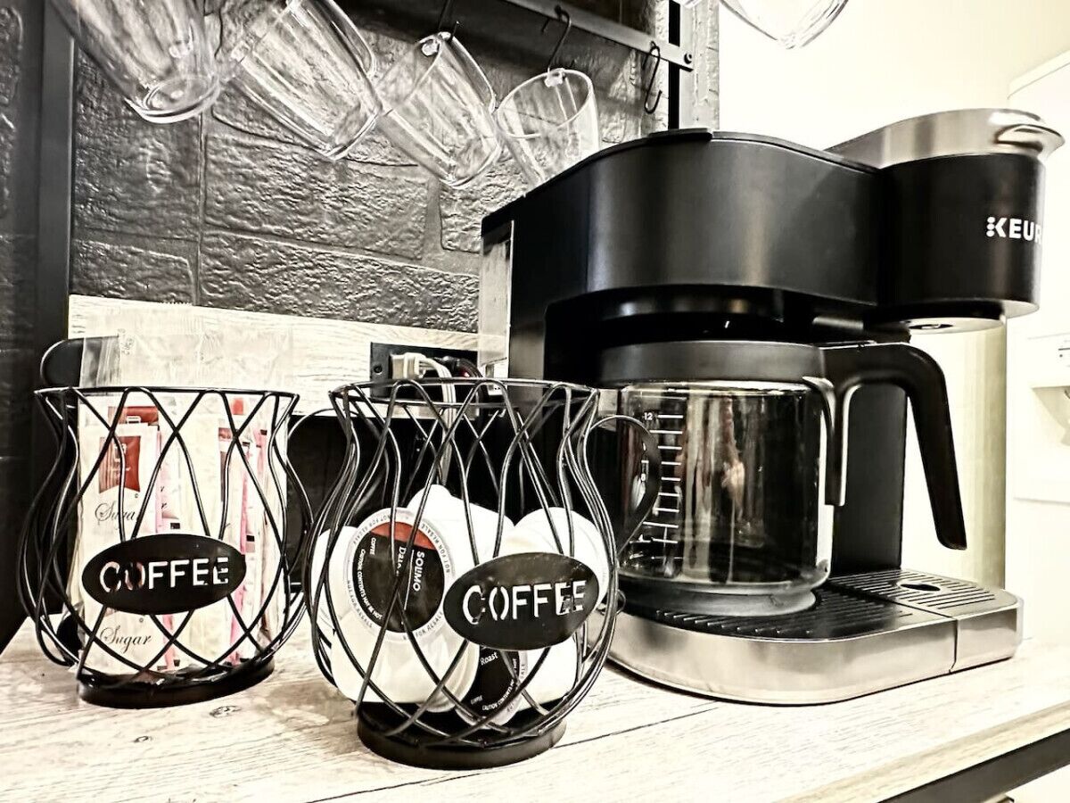 Una cafetera sobre una encimera de cocina con dos cestas de café que contienen sobrecitos de azúcar.