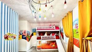 Habitació amb lliteres i tobogan, parets de ratlles i cortines de colors.