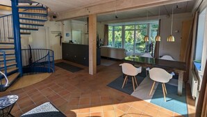 Ein geräumiger Wohnbereich mit einer blauen Wendeltreppe, einer Küche mit großen Fenstern und einem Essbereich mit modernen Stühlen.