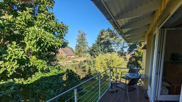 Ein Balkon mit Tisch und Stühlen, mit Blick auf einen Garten und ein Haus in der Ferne.