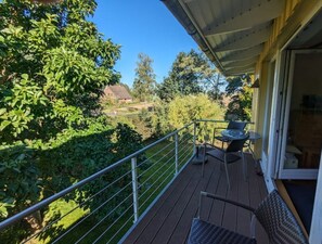 Un balcón con mesa y sillas, con vistas a un jardín y una casa a lo lejos.