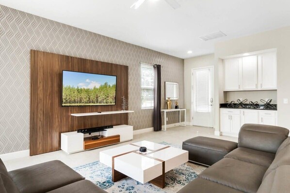 A modern living room with a flat-screen TV, a sofa, a coffee table, and a kitchen area with cabinets and a countertop.