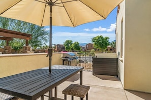 An outdoor patio with a table, an umbrella, and a grill. - Verdant Views & Amenities Near PGA West Golf (La Quinta)