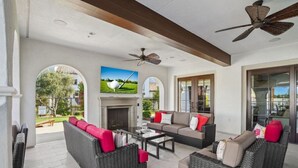 A spacious living area with wicker furniture, a fireplace, and large windows offering views of the outdoors. - Verdant Views & Amenities Near PGA West Golf (La Quinta)