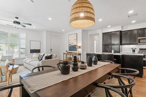 A modern kitchen with dark cabinets, a wooden dining table, and a hanging light fixture. - Verdant Views & Amenities Near PGA West Golf (La Quinta)