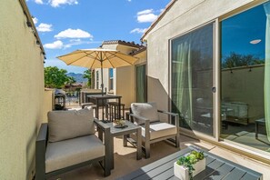 An outdoor patio with a sofa, chairs, a table, and an umbrella.