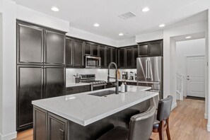 Une cuisine moderne avec des meubles de couleur sombre, des appareils électroménagers en acier inoxydable et un îlot central.