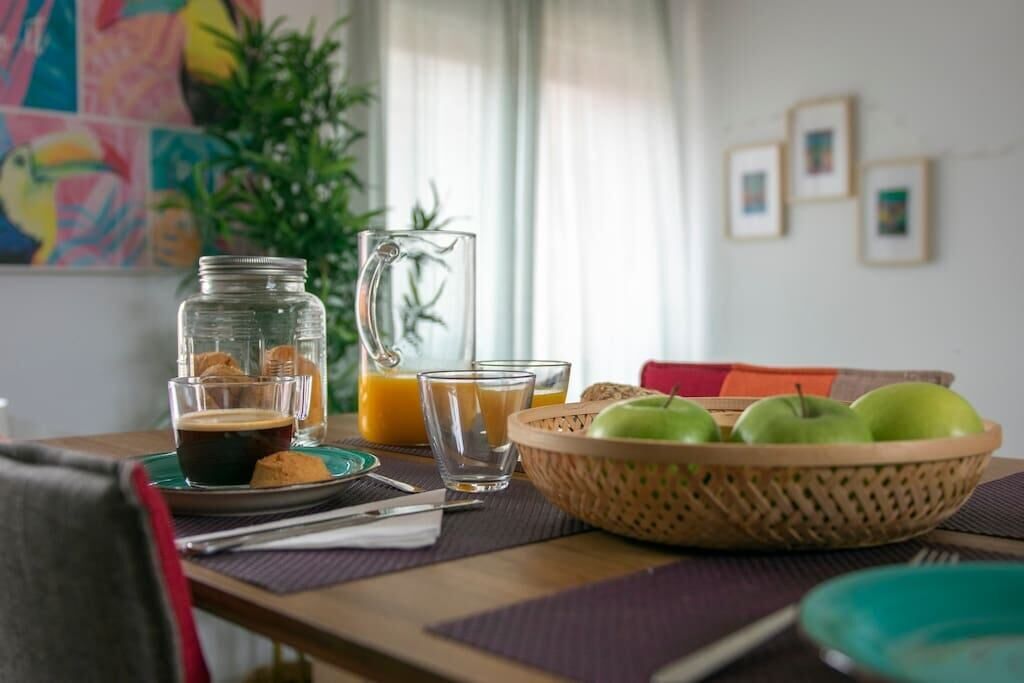 Een ontbijttafel met een koffiekop, sap, glazen, een mand appels en een karaf sinaasappelsap.