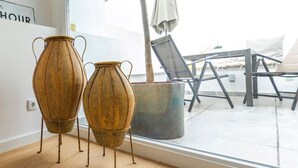 Deux vases en métal au style rustique, posés sur un plancher en bois près d’une fenêtre donnant sur un balcon et un espace de détente extérieur.