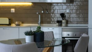 Une cuisine moderne avec des meubles blancs, une table en verre et deux plantes en pot.