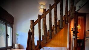 A cozy room with a wooden staircase, a white sofa with patterned cushions, a dining table with chairs, and a vase of flowers. - Casa Rural Hitohouse Bed&climb (Albarracín)