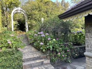 A garden pathway leading to a white archway, surrounded by lush greenery and flowering plants. - The Blossoms (Diyathalawa)