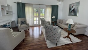 A spacious living room with a wooden floor, a sofa, two armchairs, a coffee table, and a painting on the wall. - The Blossoms (Diyathalawa)