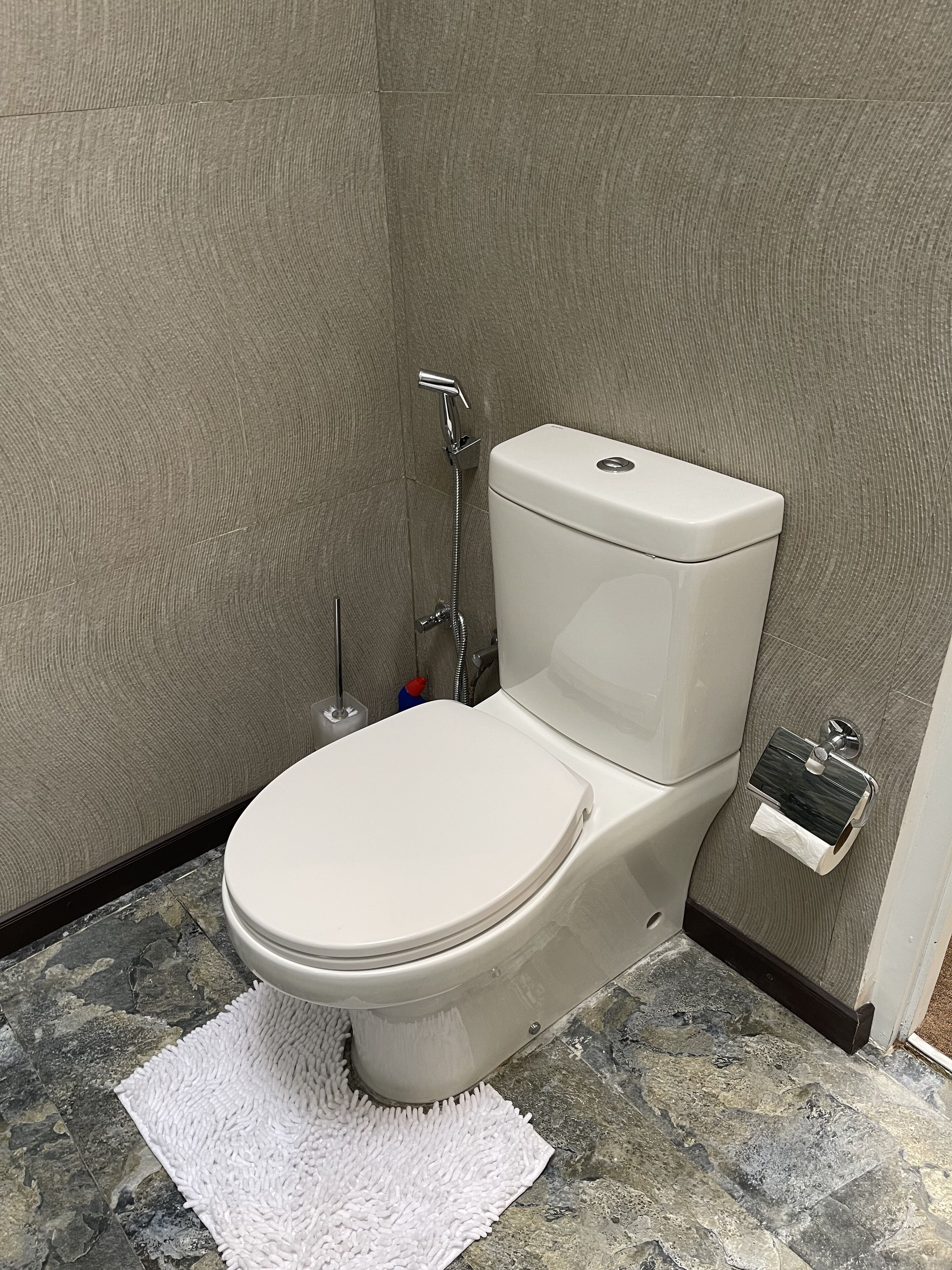 A modern bathroom with a toilet, shower, and a marble floor.