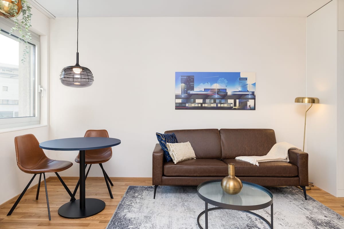 A modern living room with a brown leather sofa, two brown chairs, a round table, and a hanging pendant light.
