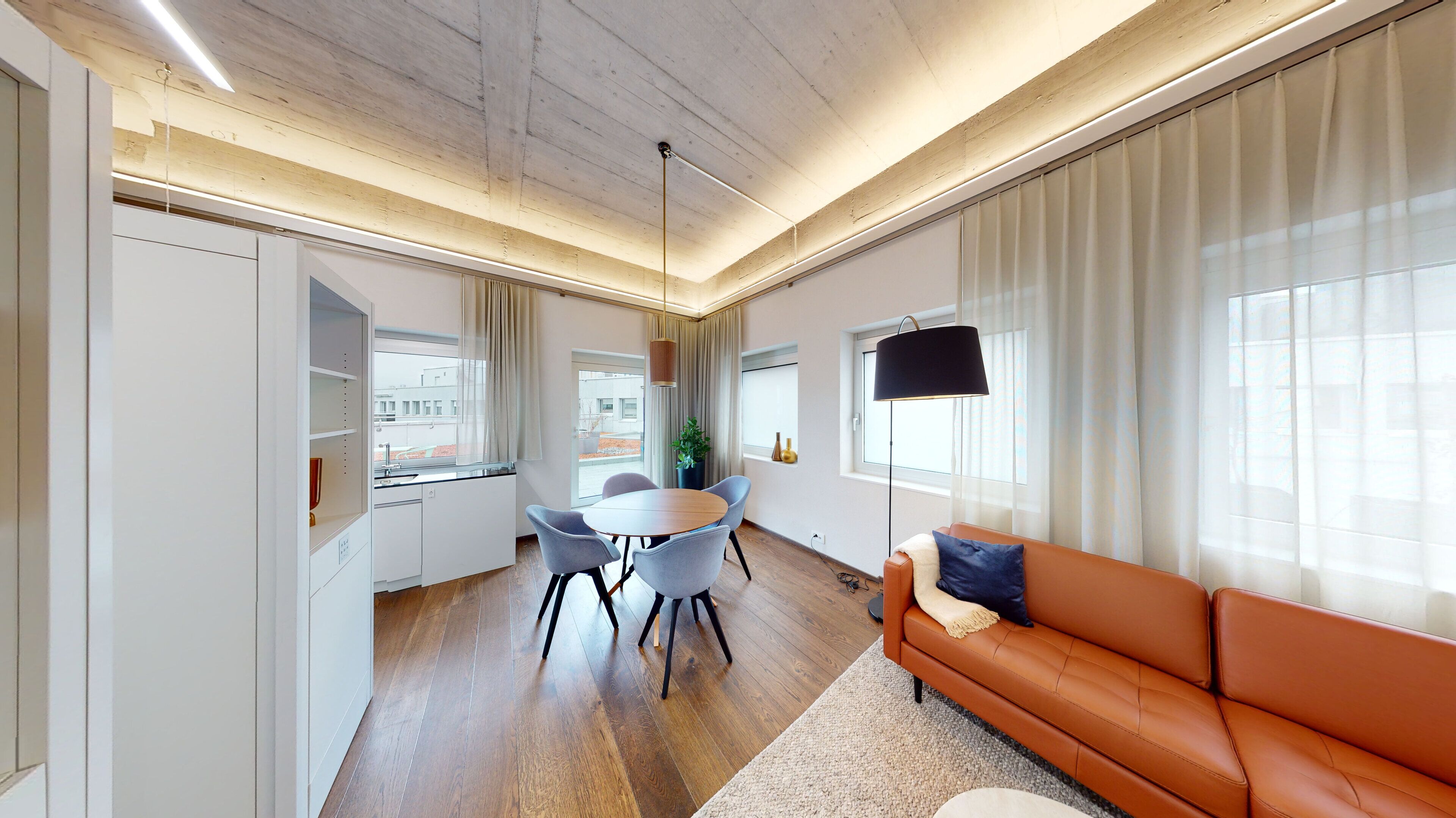 A modern living room with a wooden ceiling, a round dining table with chairs, a sofa, and a TV mounted on the wall.