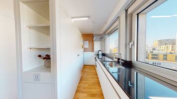 A narrow kitchen with white cabinetry, a wooden floor, and a window overlooking a cityscape.