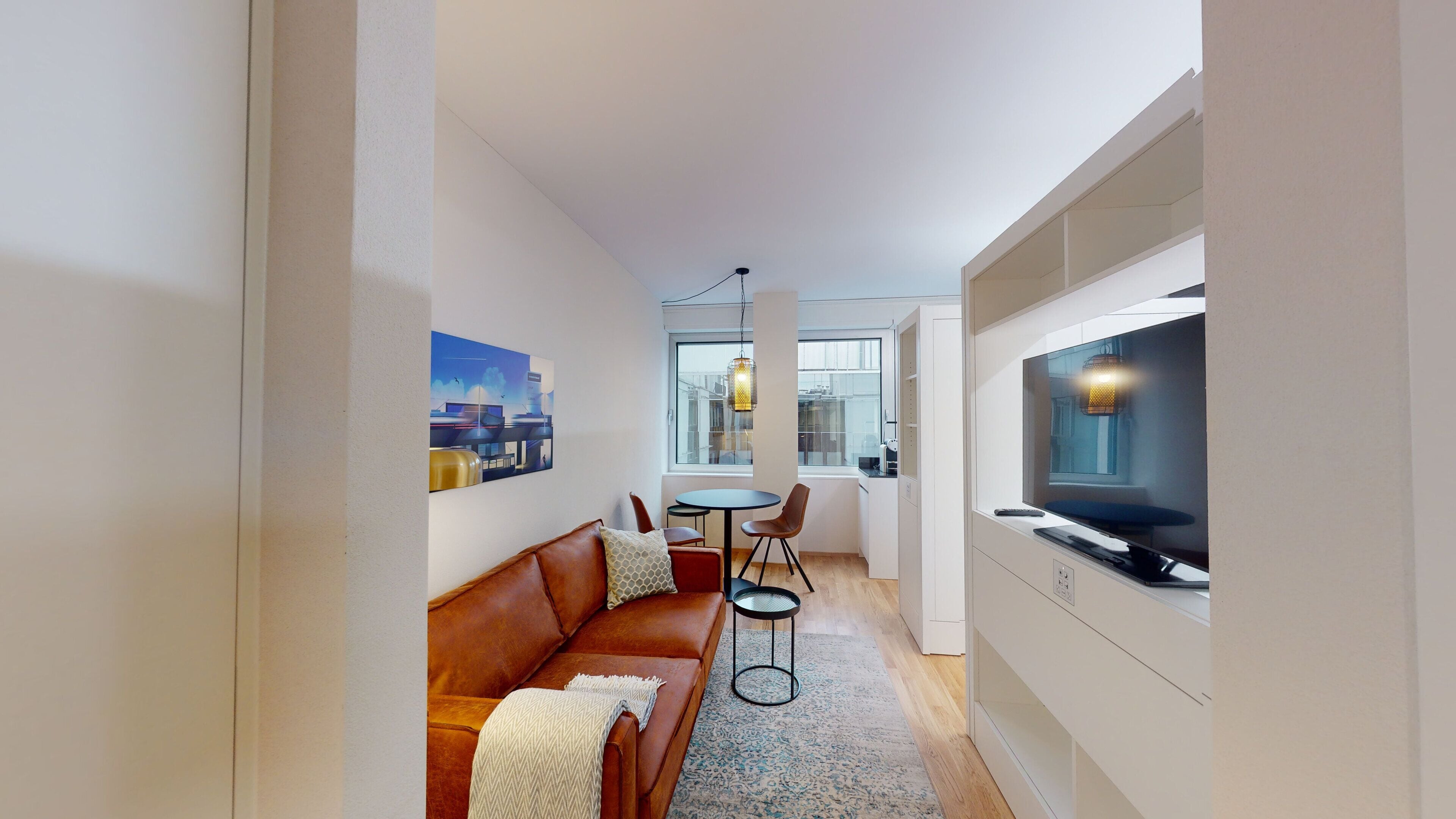 A modern living room with a brown leather sofa, a small round table, and a TV mounted on the wall.