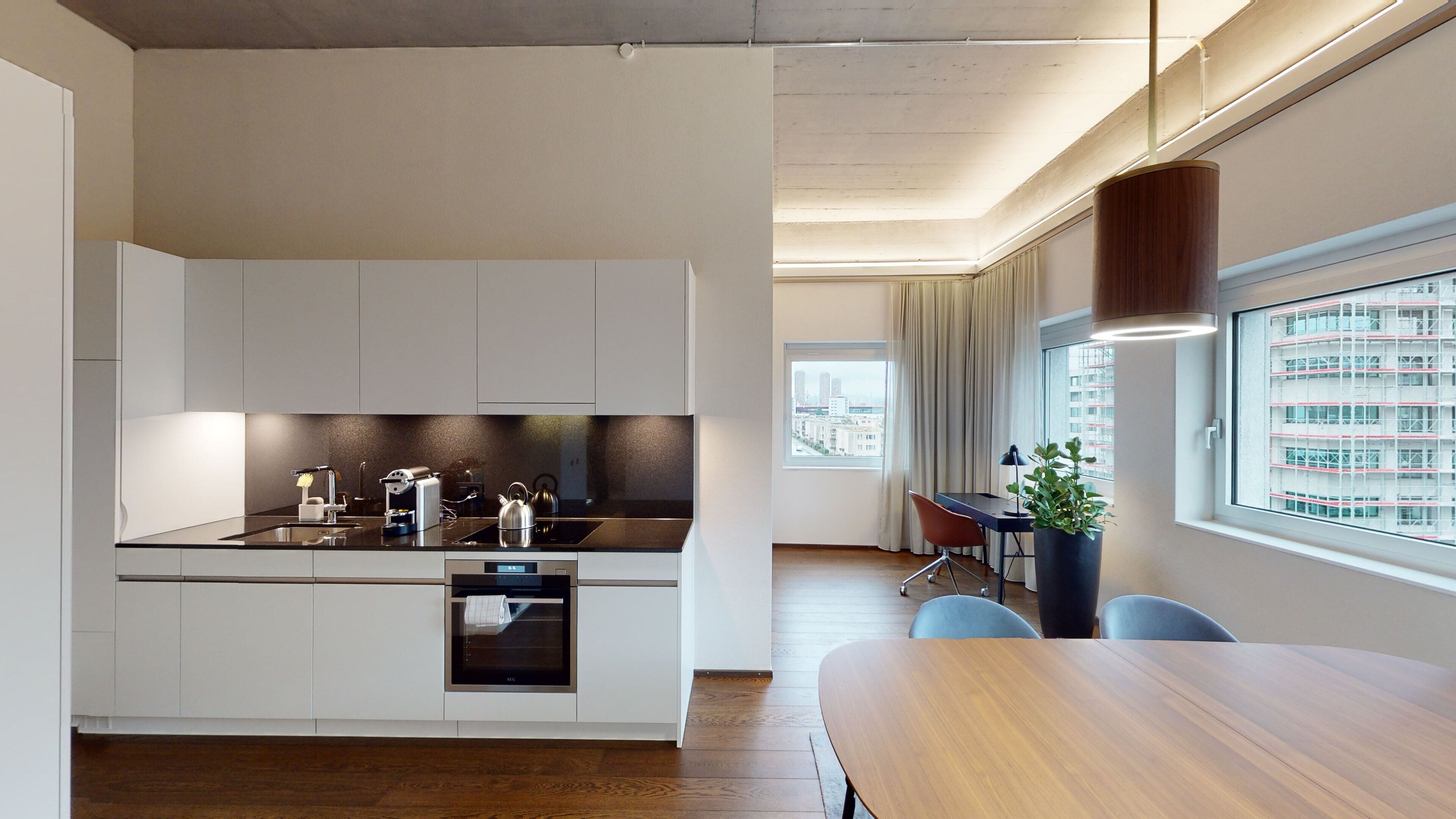 A modern kitchen with white cabinets, a built-in oven, and a dining area with a wooden table and chairs.