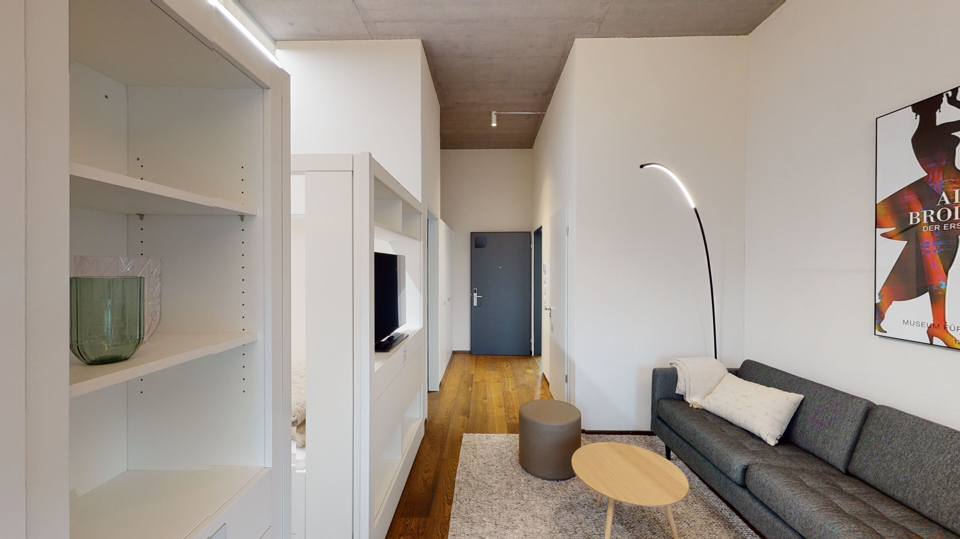A modern living room with a grey sofa, a small round table, and a bookshelf.