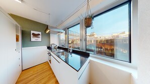A modern kitchen with a large window, wooden flooring, and a cityscape view. - LivingTown Lofts Zurich (Zürich)