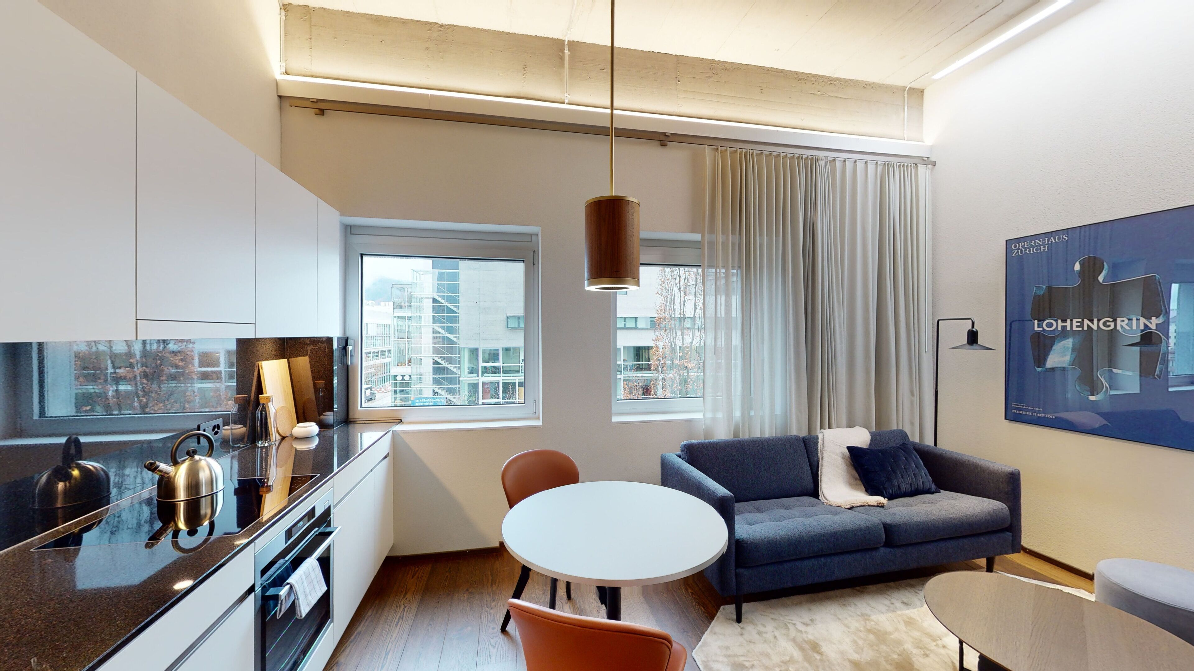 A modern living room with a sofa, a dining table, and a kitchen area with a kettle.