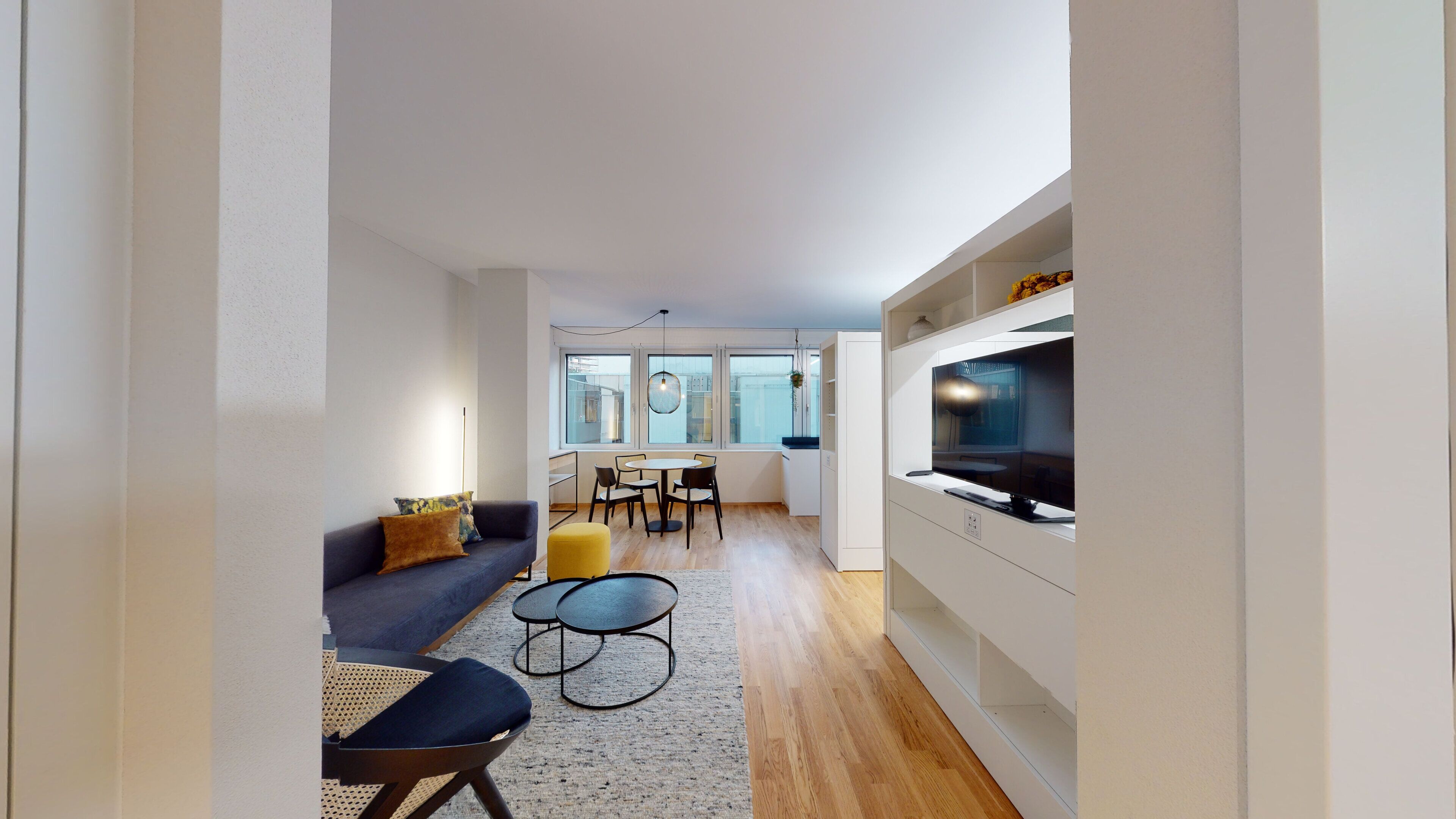 Een moderne woonkamer met een bank, salontafel en stoelen, een eethoek met tafel en stoelen, en een keuken met een televisie.