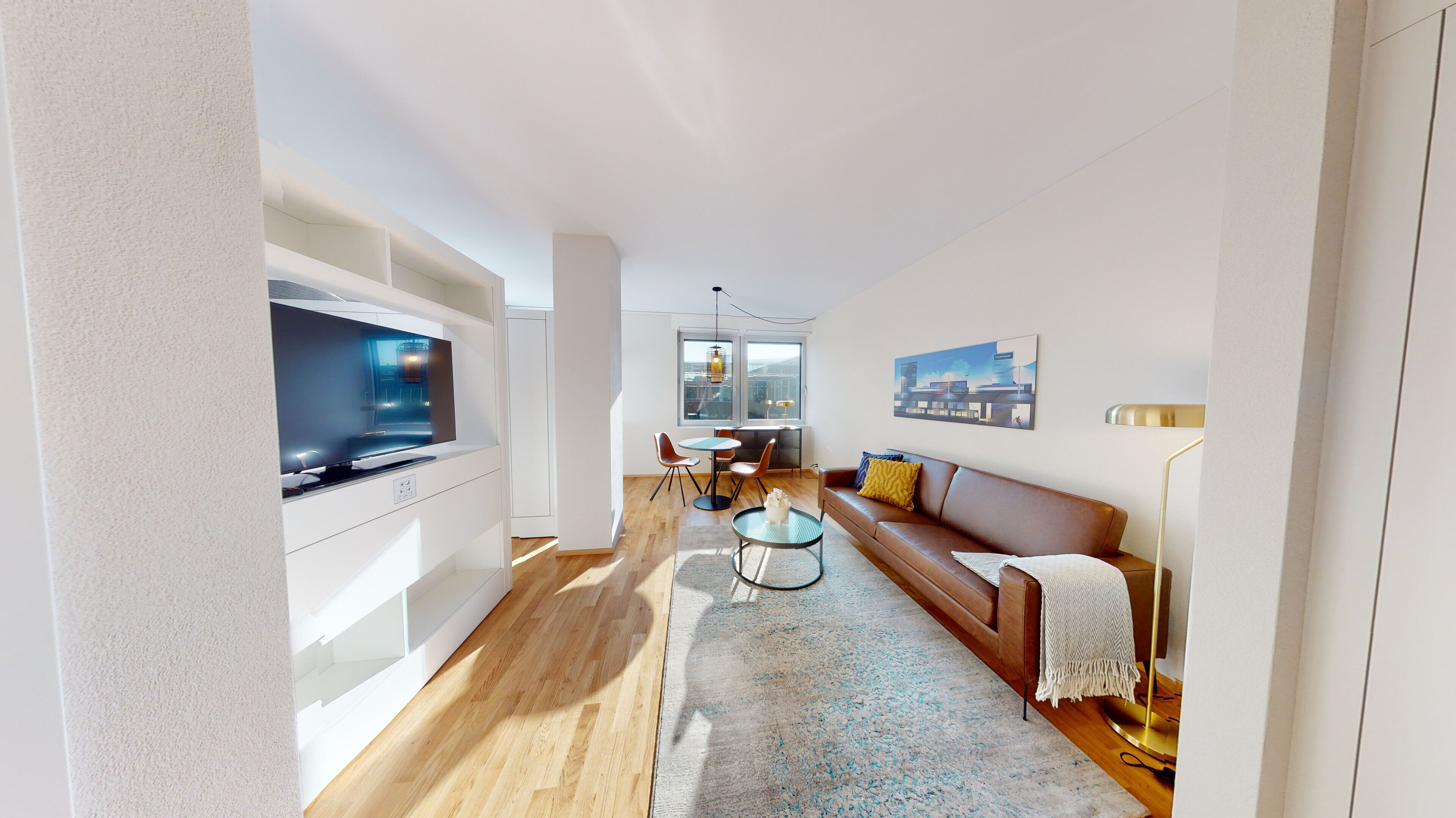 Ein modernes Wohnzimmer mit Flachbildfernseher, braunem Ledersofa, Couchtisch und Essbereich mit Tisch und Stühlen.