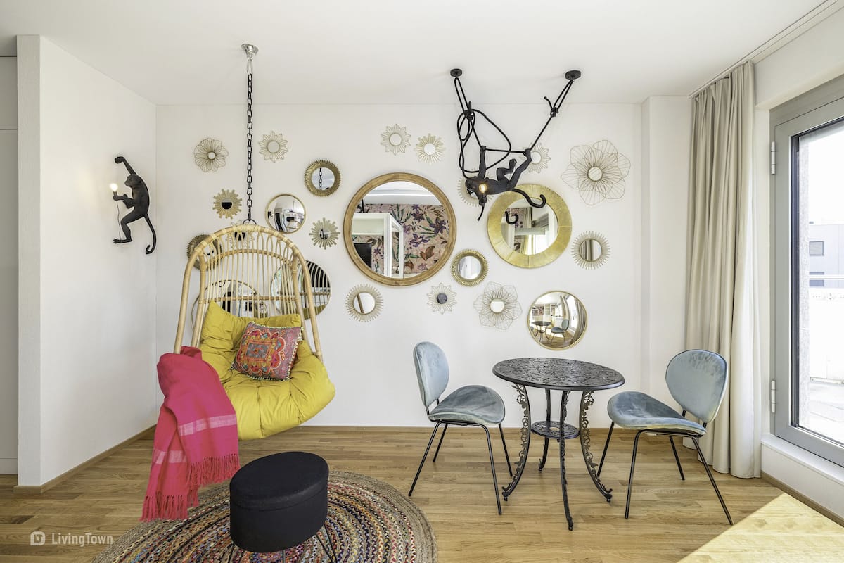 A room with a hanging chair, a small round table, two chairs, and a large mirror on the wall.