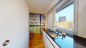 A modern kitchen with a wooden floor, a stainless steel sink, and a window with a city view. - LivingTown Lofts Zurich (Zürich)