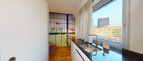 A modern kitchen with a wooden floor, a stainless steel sink, and a window with a city view.