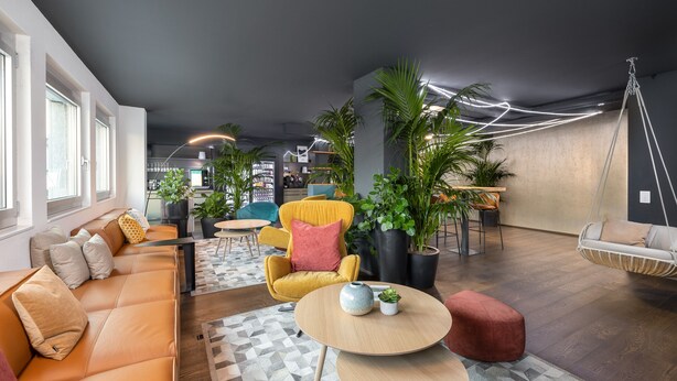 A modern lounge area with a sofa, armchairs, a hanging chair, and a round table. - LivingTown Lofts Zurich (Zürich)