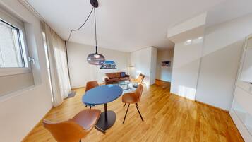 Een moderne woonkamer met een ronde blauwe tafel, leren fauteuils, een bank en een hanglamp.