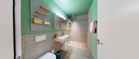 Une salle de bain moderne avec un mur vert, un lavabo blanc, des toilettes et une douche.