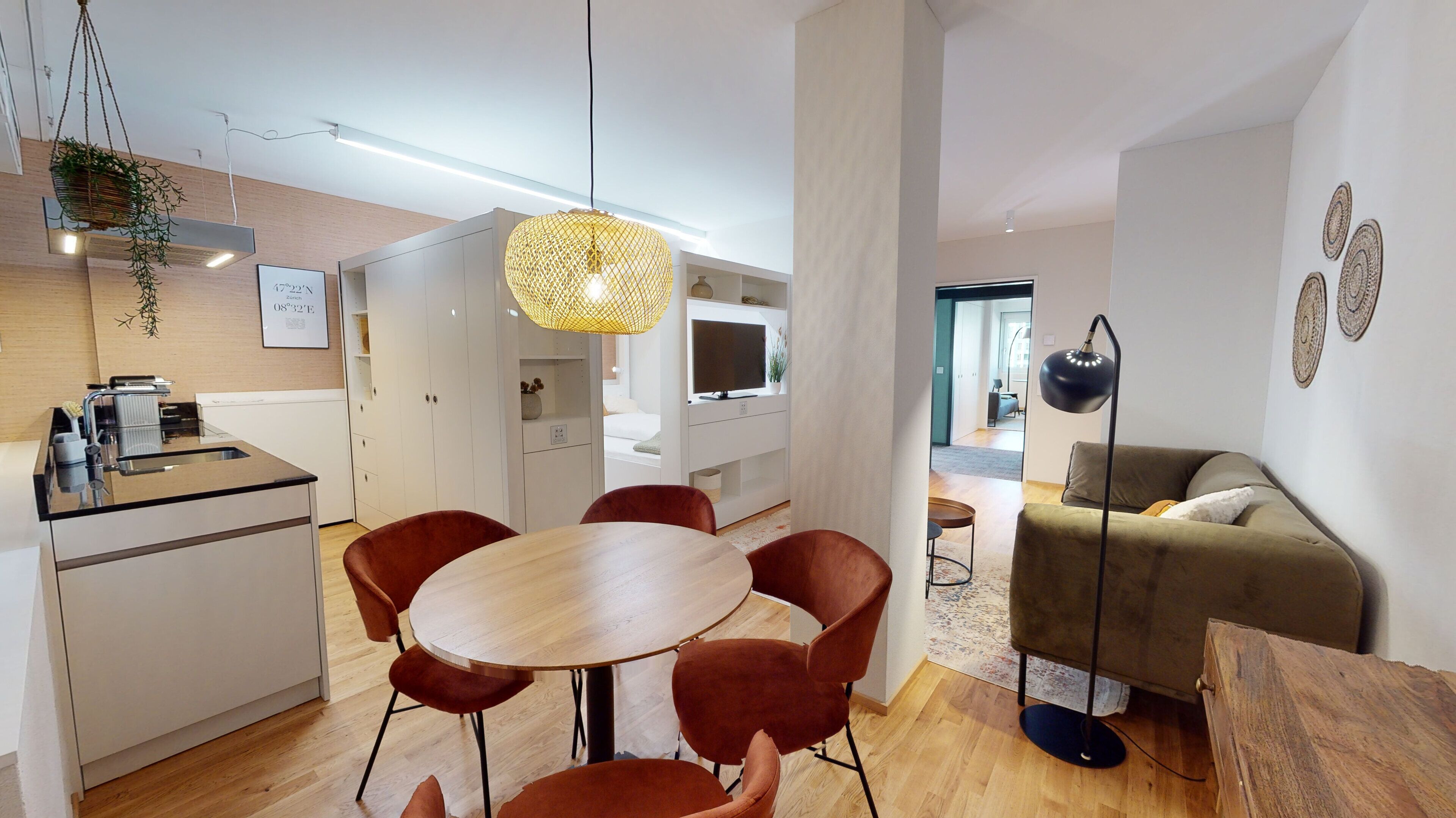 A modern kitchen with white cabinets, a dining table with red chairs, and a hanging plant.