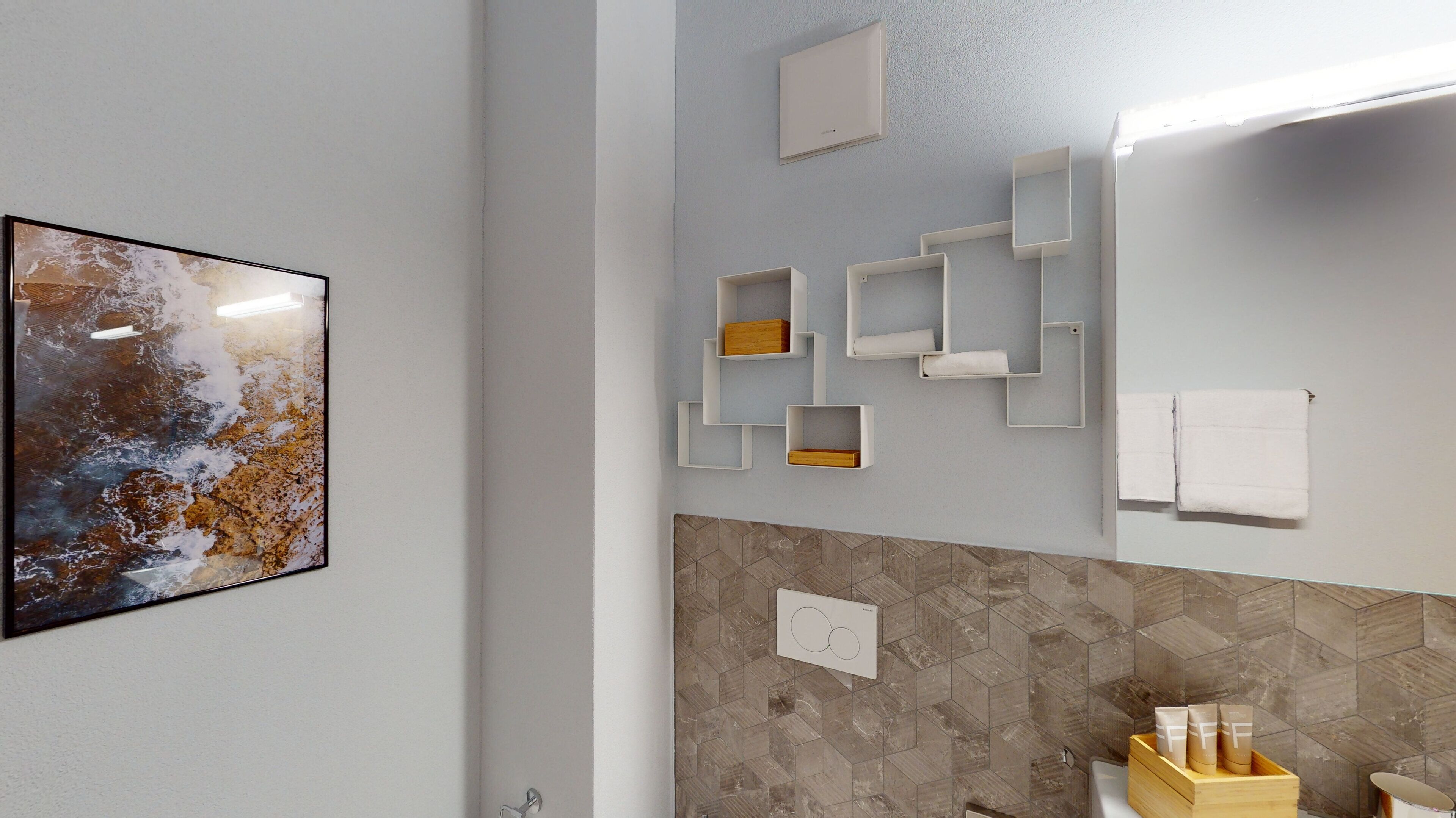 A modern bathroom with a geometric tile backsplash, a framed abstract painting, and a white towel rack.